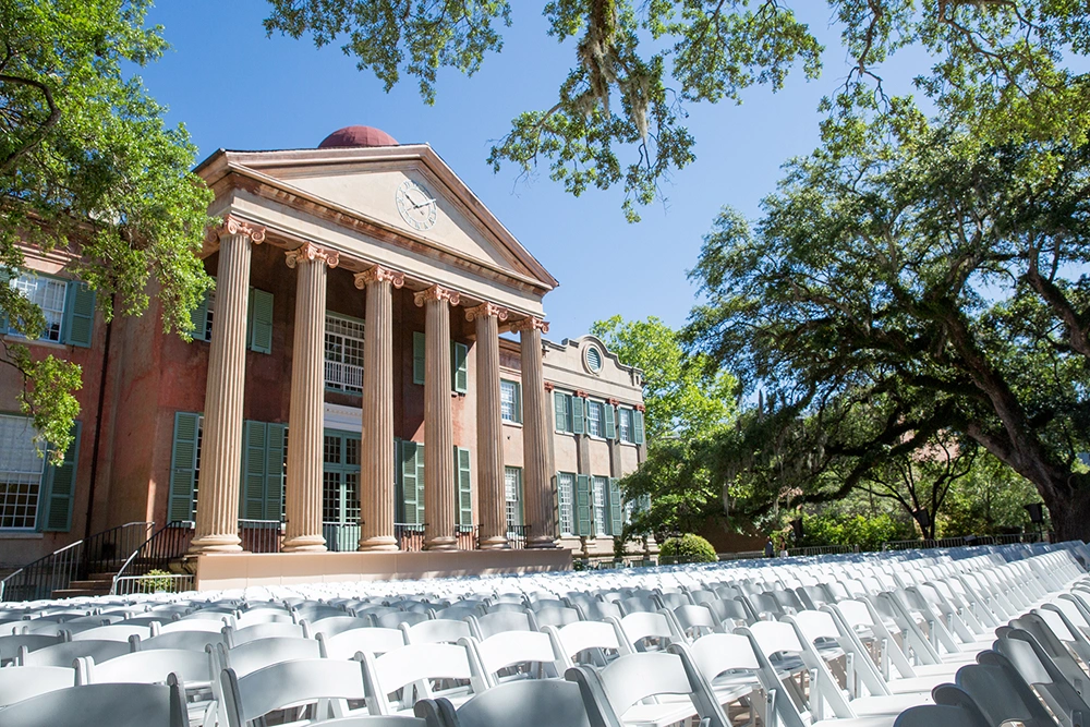 Long rows of white folding chairs set outdoors in front of facade of colonnaded university building