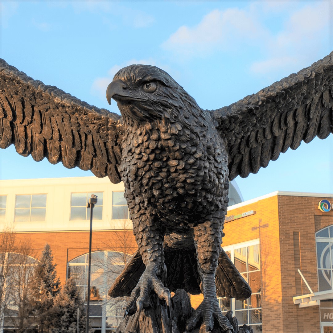 Image of Monmouth University building with large statue of hawk mascot in foreground