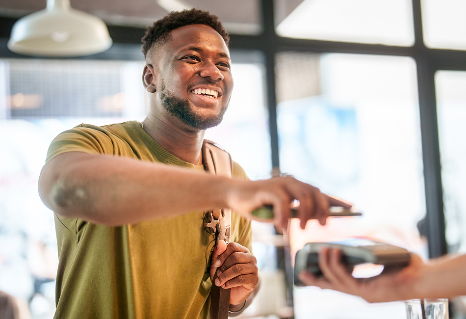 A smiling college student uses his mobile device to make a contactless payment at a cafeteria.