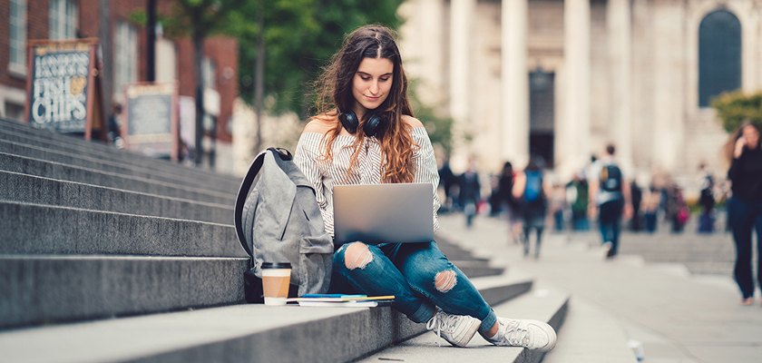 A student sits on outdoor steps while working on a laptop.
